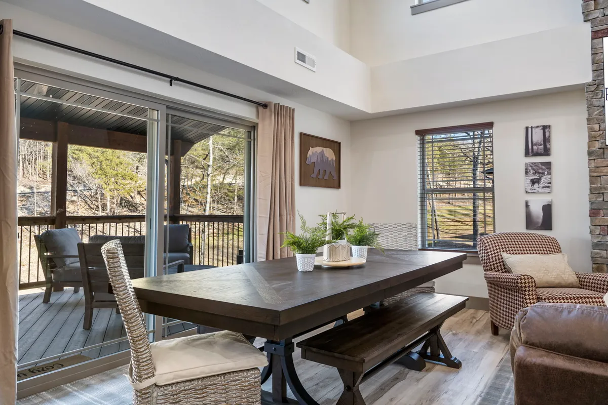 A stylish dining area featuring a large table set for a meal, complemented by decorative wall art and a sliding glass door that opens to natural woodland views. The room is filled with warm light, and the setting is perfect for family meals or festive gatherings.