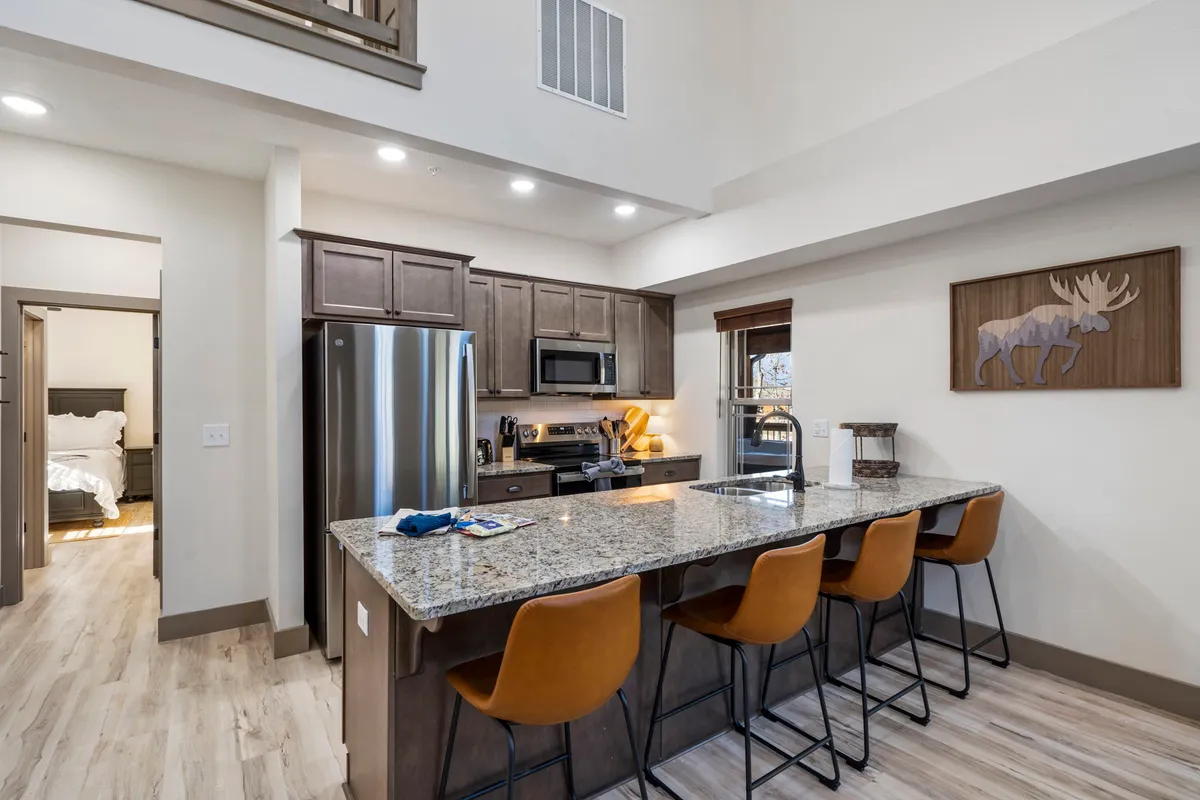 This image captures a modern kitchen with granite countertops, bar stools, stainless steel appliances, and charming moose artwork. The kitchen's open layout invites conversation and togetherness, and the sleek appliances are ready for any meal prep. The cozy yet stylish decor blends contemporary convenience with rustic cabin character.