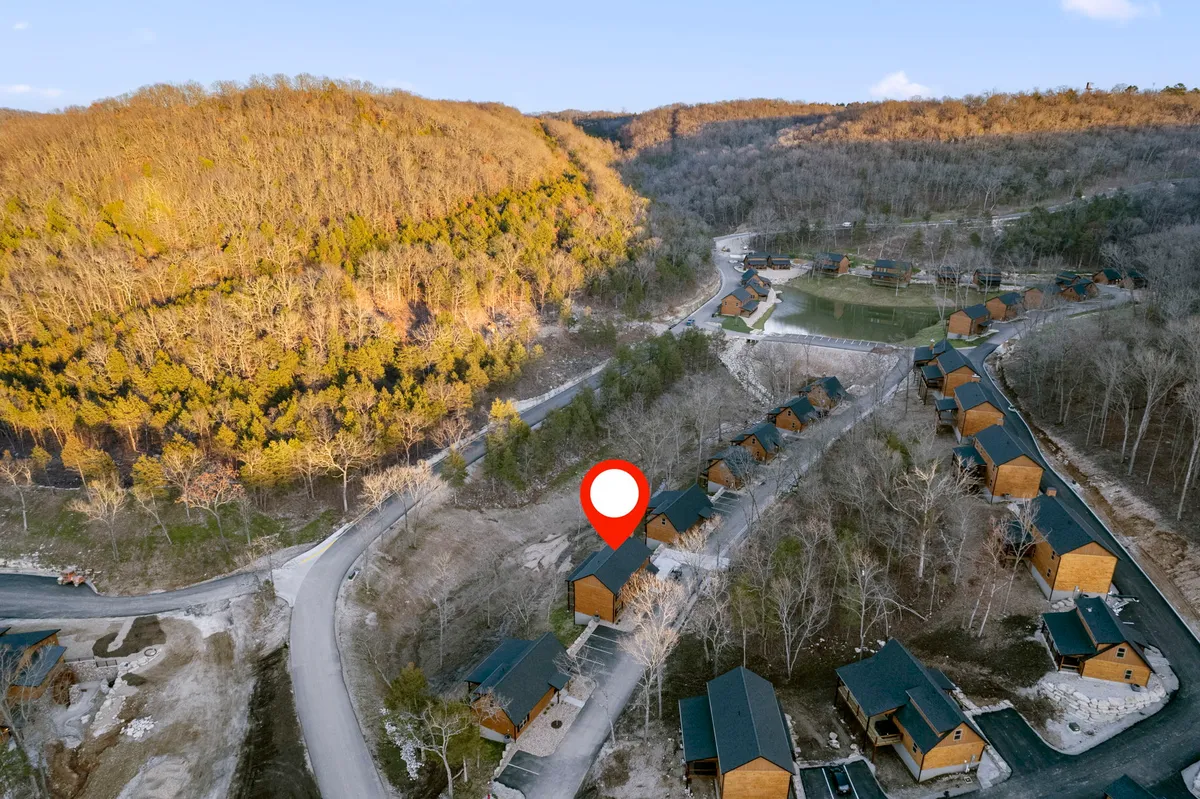 This image features a cluster of cozy wooden cabins nestled in a lush, forested environment with a winding road leading through the trees. The scene is tranquil, emphasizing the natural setting and the proximity to hiking and nature walks.