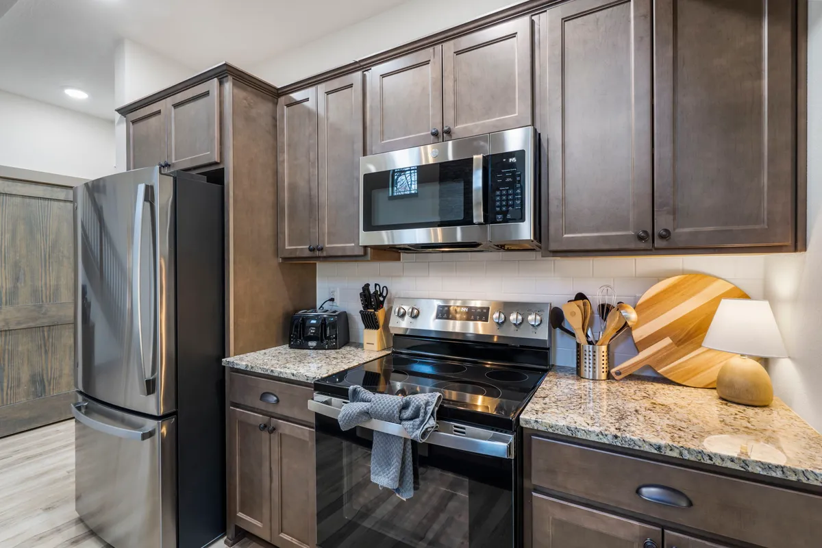 A bright kitchen scene featuring gleaming stainless steel appliances, a granite countertop, a wooden cutting board, and a variety of kitchen utensils. The natural lighting and warm accents create an inviting atmosphere that encourages cooking and communal dining.