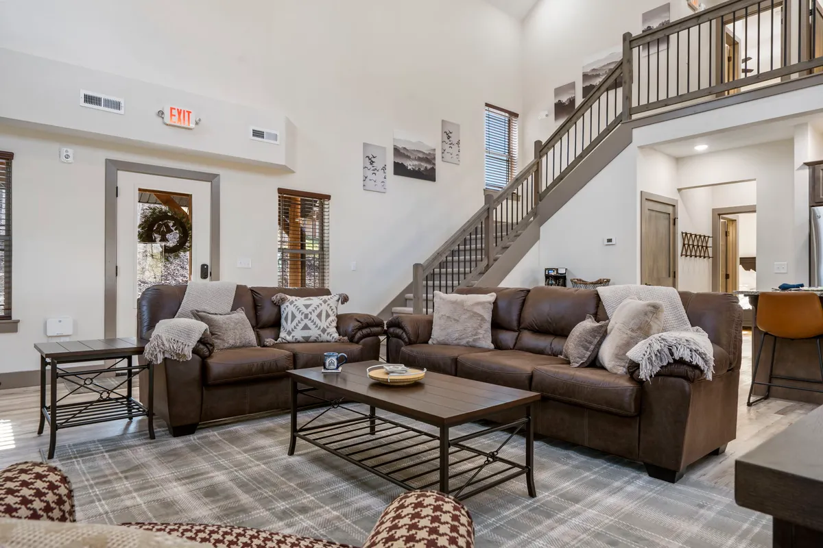 A cozy living room scene with plush leather sofas, a coffee table, and a staircase leading to the upper level. The layout encourages conversation and togetherness, with soft lighting and comfortable furnishings that invite relaxation after a day of adventure.