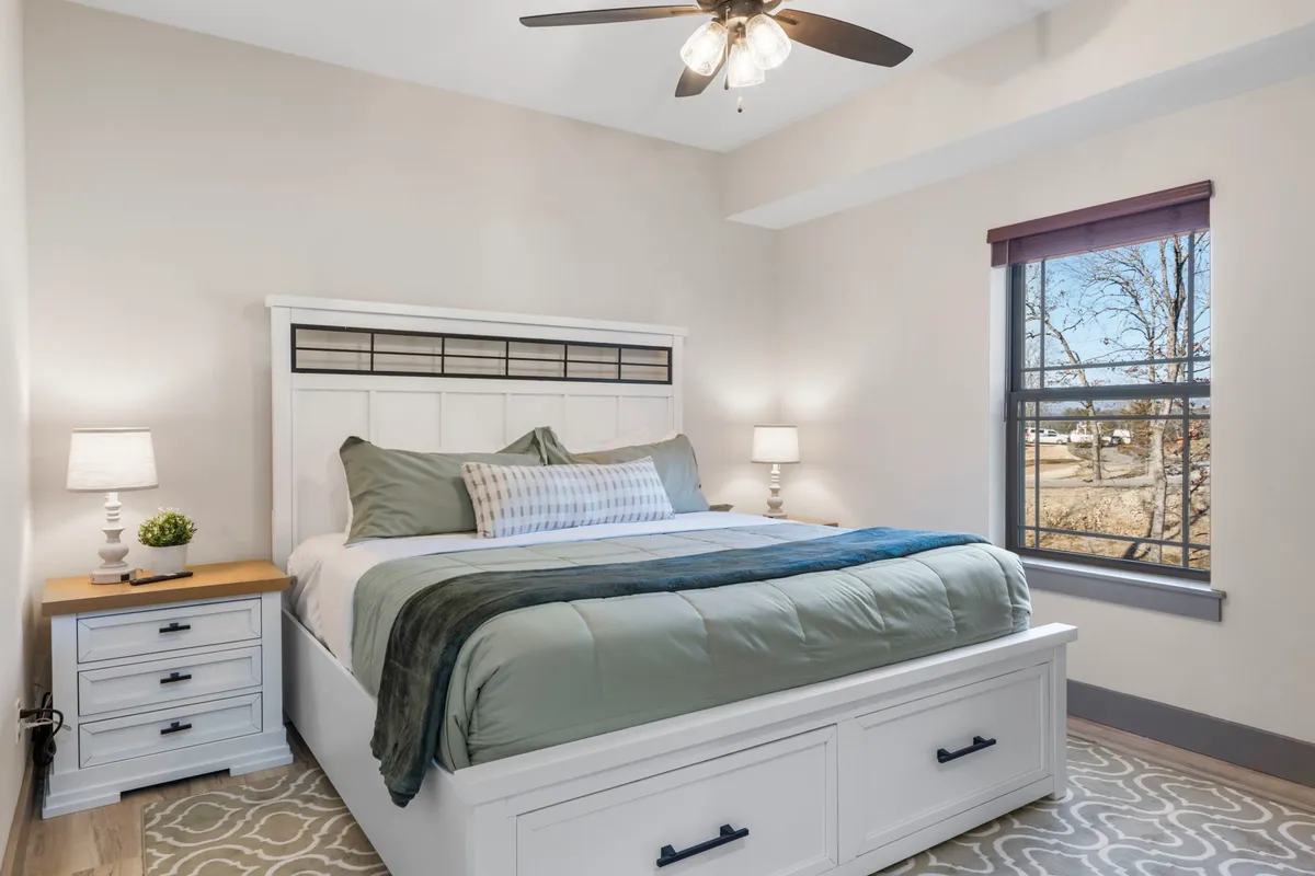 A sunlit king bedroom featuring a plush bed adorned with decorative pillows, a cozy nightstand with a lamp, and a window inviting natural light into the space. The room exudes tranquility, perfect for unwinding after a day of adventure.