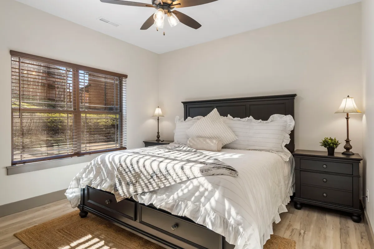 A peaceful king bedroom with a comfortable bed, soft linens, a bedside lamp, and a window allowing warm natural light to filter in. The room is set up for both relaxation and quiet reading, embodying a sense of calm.