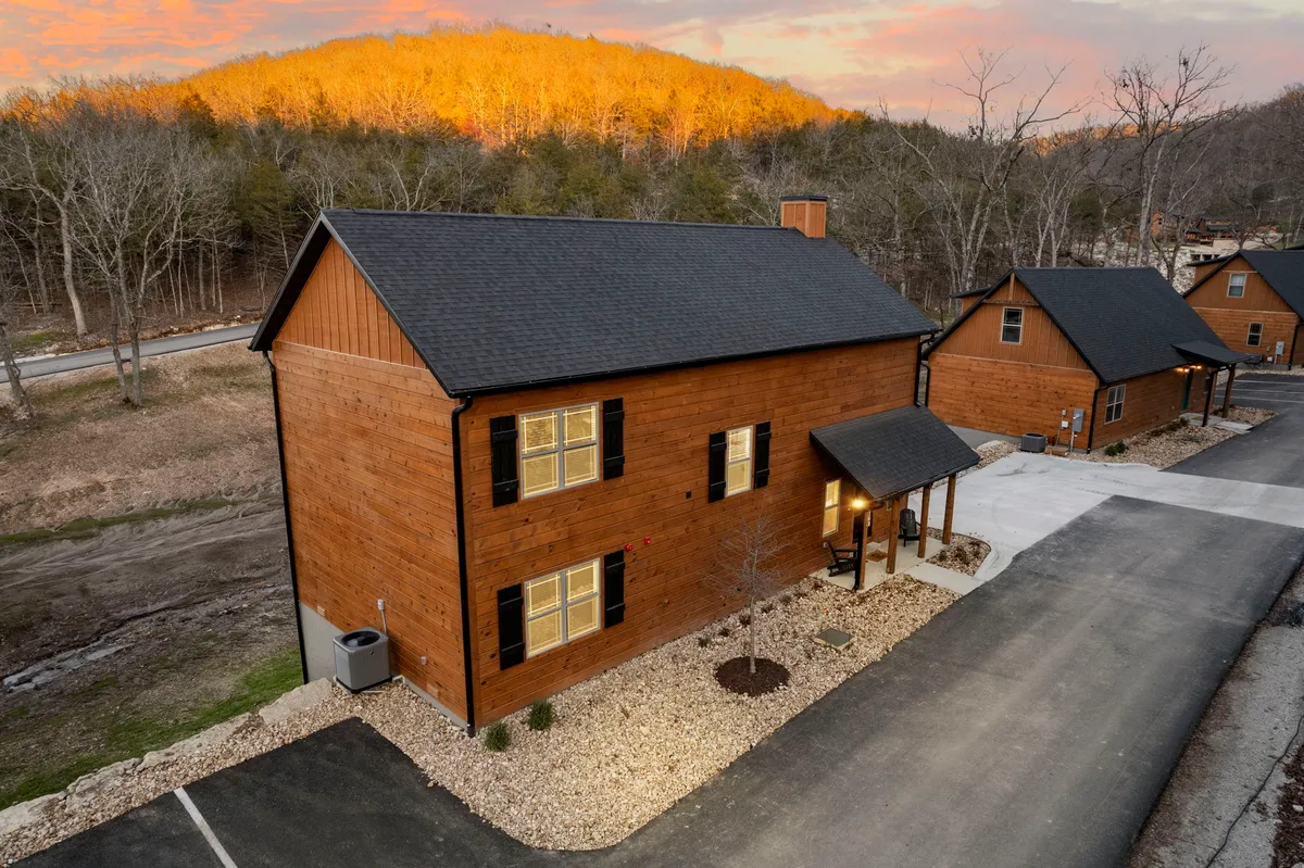 A beautiful exterior shot of a wooden cabin at sunset, surrounded by lush nature and hills. The cabin features large windows and a spacious porch, inviting guests to relax and enjoy the peaceful natural surroundings. The warm glow of the sunset enhances the sense of tranquility and retreat.