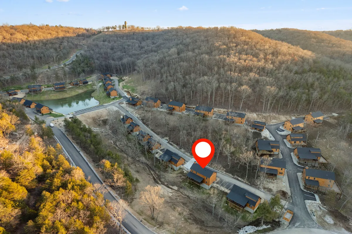 A tranquil lakeside area with a cluster of cabins, a winding road, and a forested backdrop. The lake sits peacefully in the foreground, inviting guests to enjoy hiking, fishing, and nature walks.