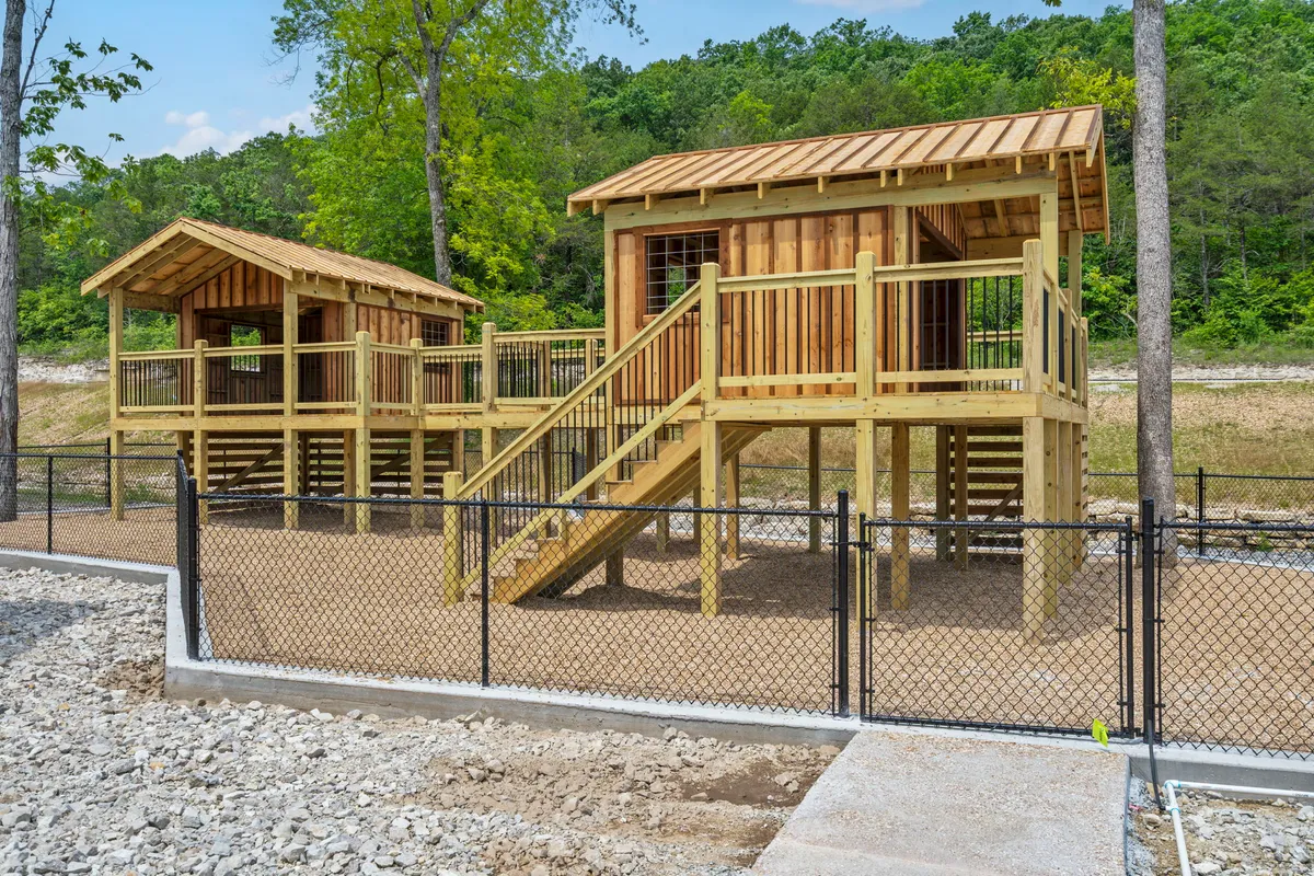 A vibrant wooden play structure stands amidst lush greenery and a fenced area, inviting children and families to engage in imaginative play and outdoor exploration.