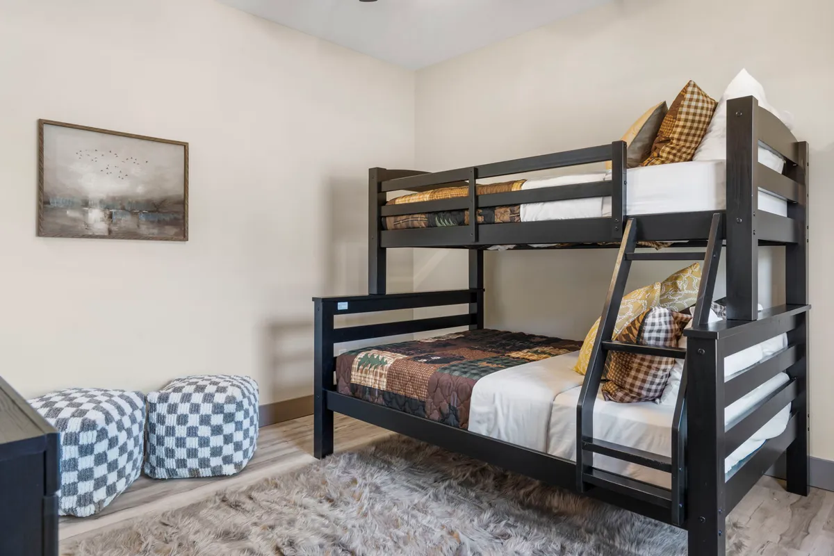 A playful bunk room designed for children, with multiple bunk beds, plaid pillows, cheerful artwork, and checkered poufs. The space is colorful, cozy, and full of personality—perfect for sleepovers and group fun.